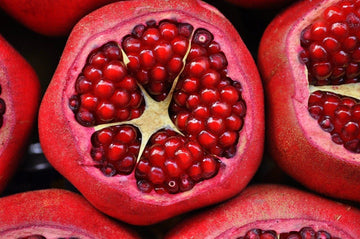 Close-up of several halved pomegranates showing clusters of red, glossy seeds inside.